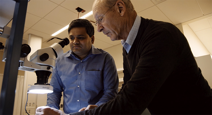 Steve Axelrod, right, and Anand Navalgund working together beside a microscope in the lab.