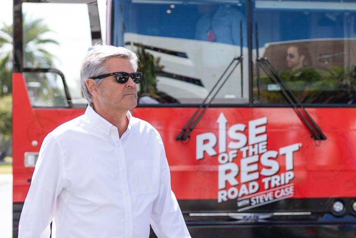 Steve Case wearing sunglasses beside the red Rise of the Rest road-trip bus