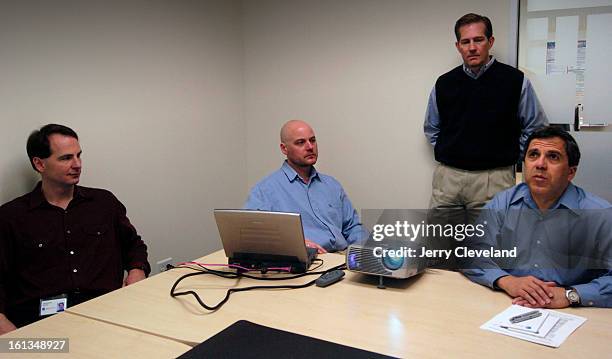 Steve Goodbarn stands behind three Secure64 colleagues gathered around laptops during a software demonstration in 2005.