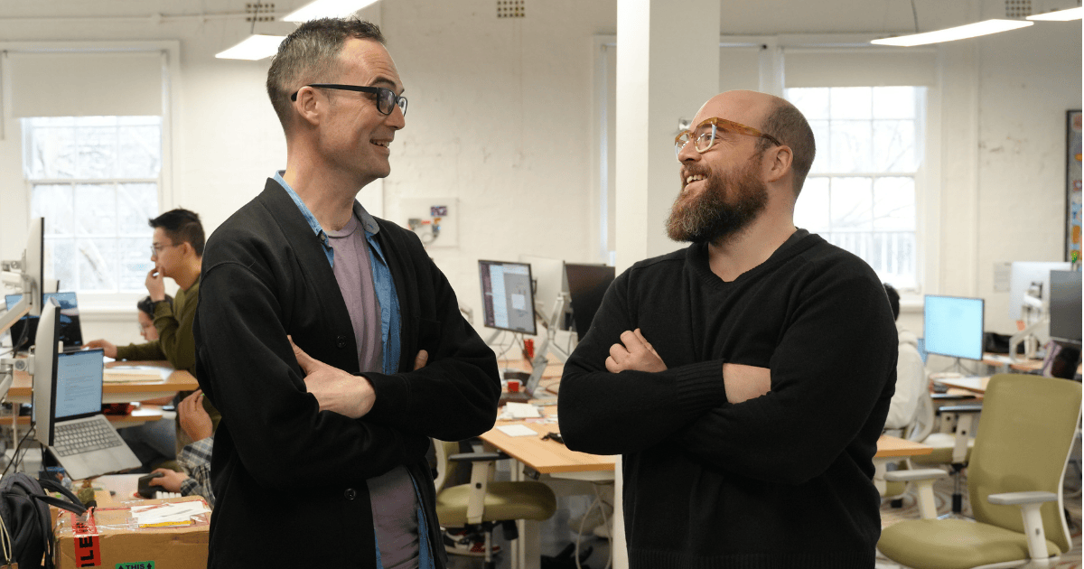 Jamie Hall and Steve Hind talking in an open office with colleagues working behind them
