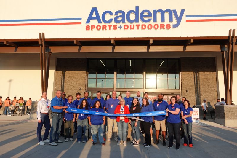 Academy employees and guests gather behind a blue ribbon outside a new store