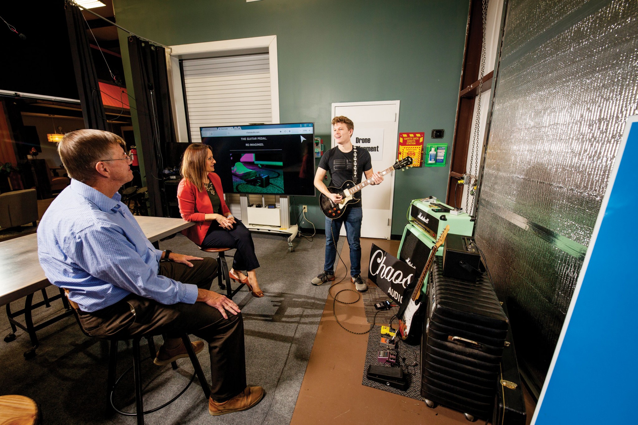 Steve Millaway, seated at left, and Kelly Reeser watch Landon McCoy demonstrate a guitar and Chaos Audio pedal