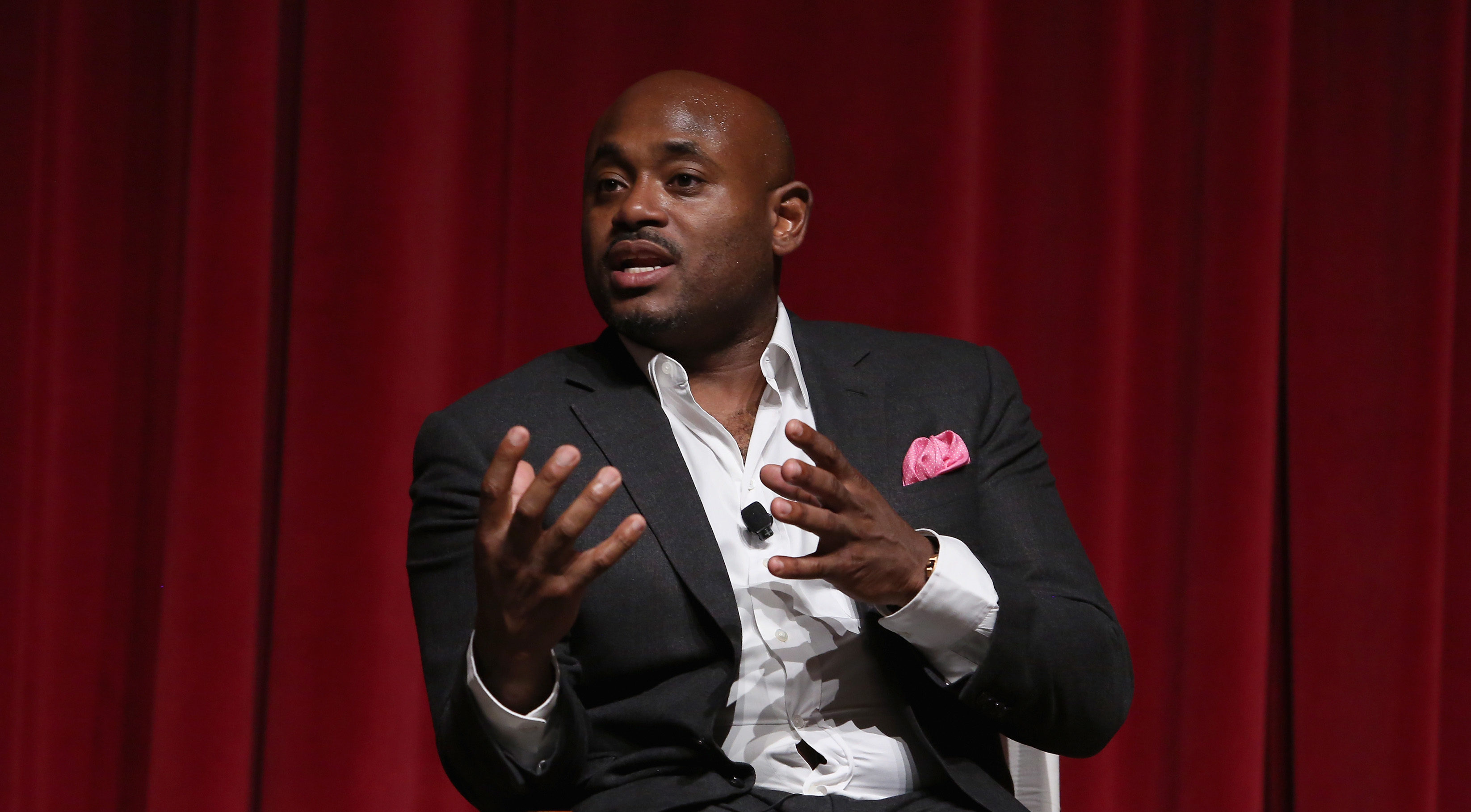 Steve Stoute speaking onstage in front of deep red curtains