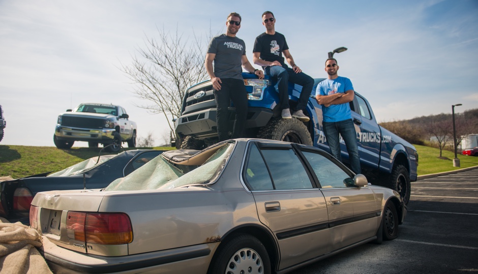 Turn5 team members pose on a lifted pickup above two crushed cars