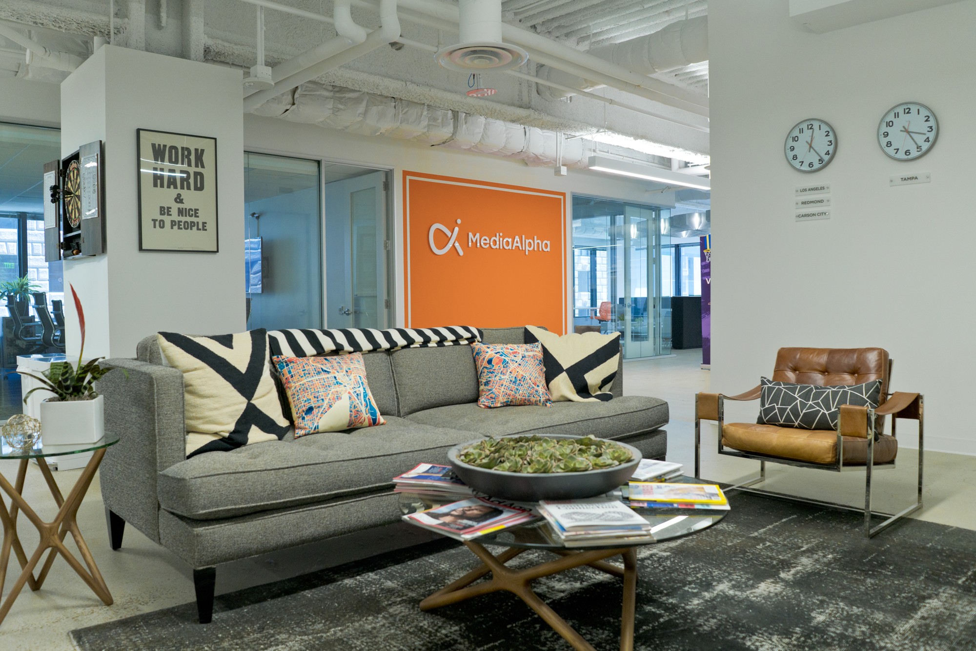 MediaAlpha's former downtown Los Angeles office, with a sofa, orange company wall and a framed work hard and be nice to people sign