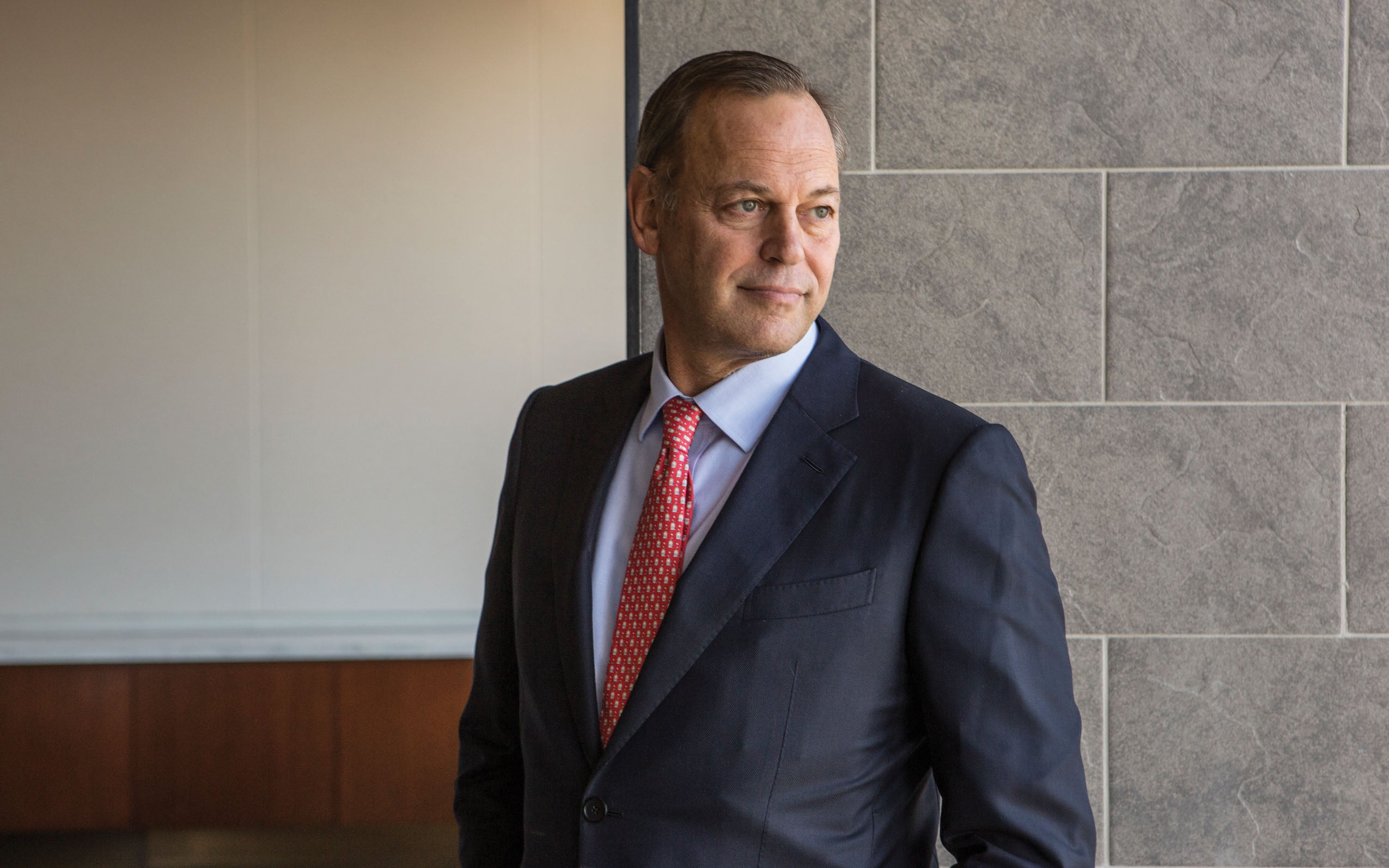 Steven Klinsky in a suit and red tie, photographed beside a stone wall