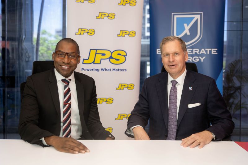 Jamaica Public Service CEO Hugh Grant, left, seated with Steven Kobos, right, in front of their companies’ banners.