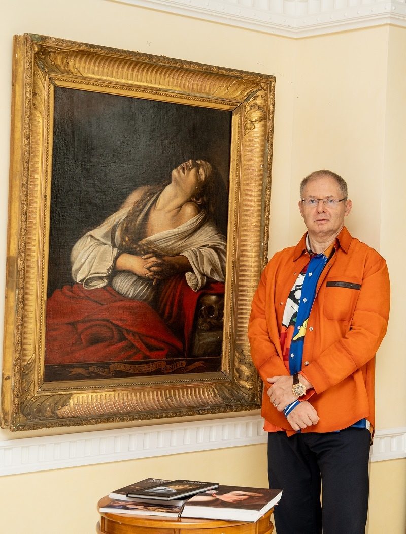Steven Maksin in an orange jacket beside the framed Mary Magdalene in Ecstasy painting from his family collection