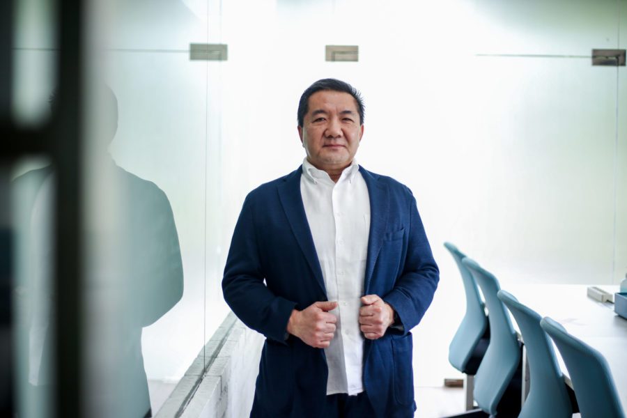 Stevensang standing beside a glass wall in an office, wearing a navy jacket