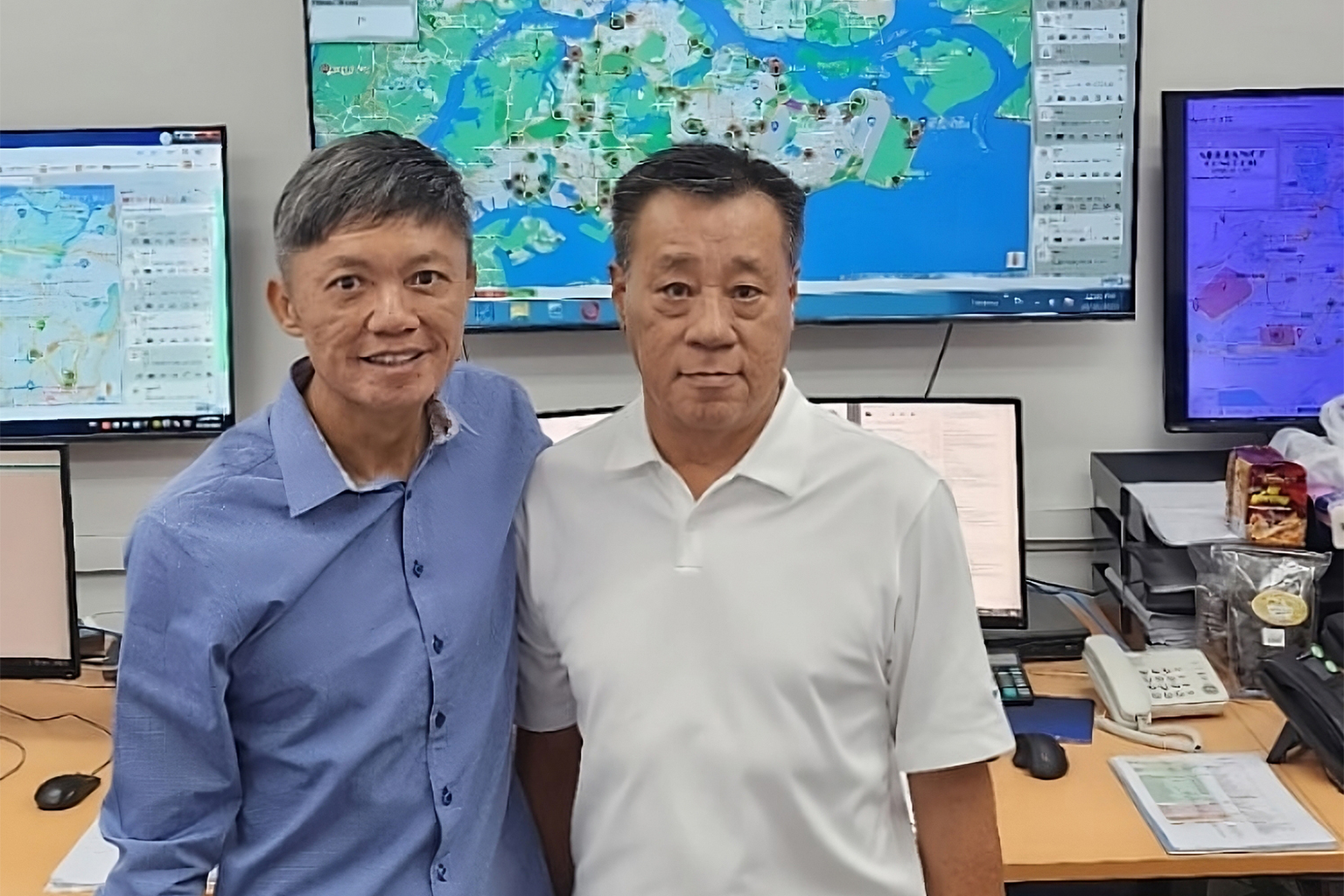 Stevie Ooi, left, beside a colleague in front of fleet maps and computer screens