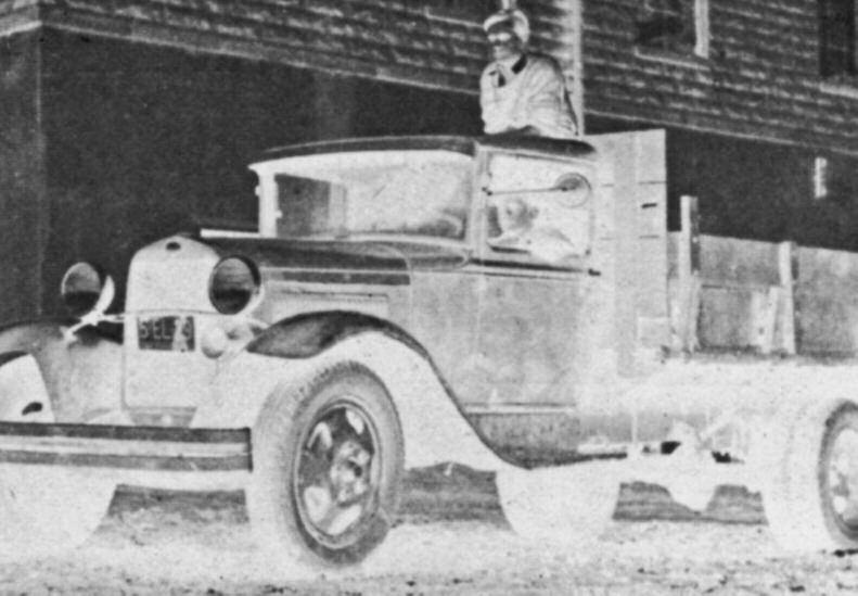 Archival photograph of young Stewart Bainum standing behind a work truck