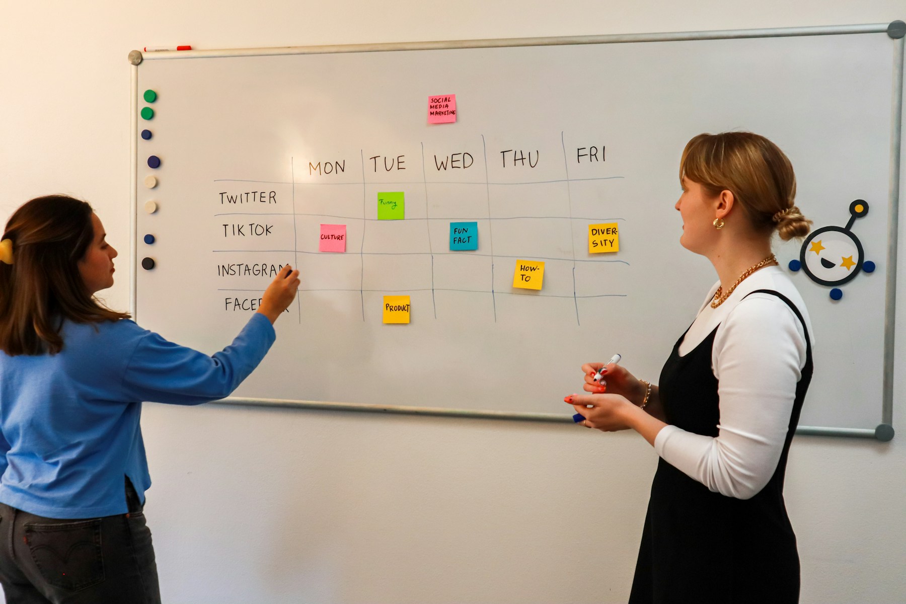 Two colleagues planning a marketing calendar with sticky notes on a whiteboard