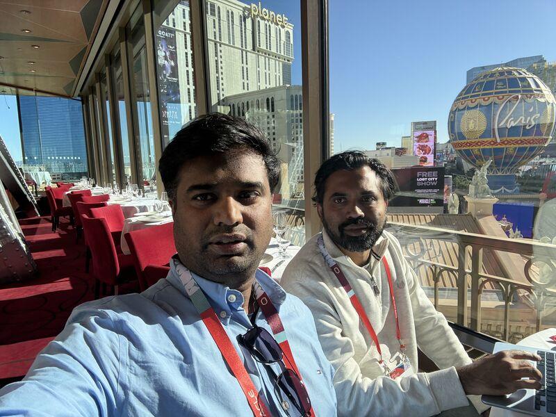 Two attendees wearing event lanyards seated beside a window overlooking the Las Vegas Strip