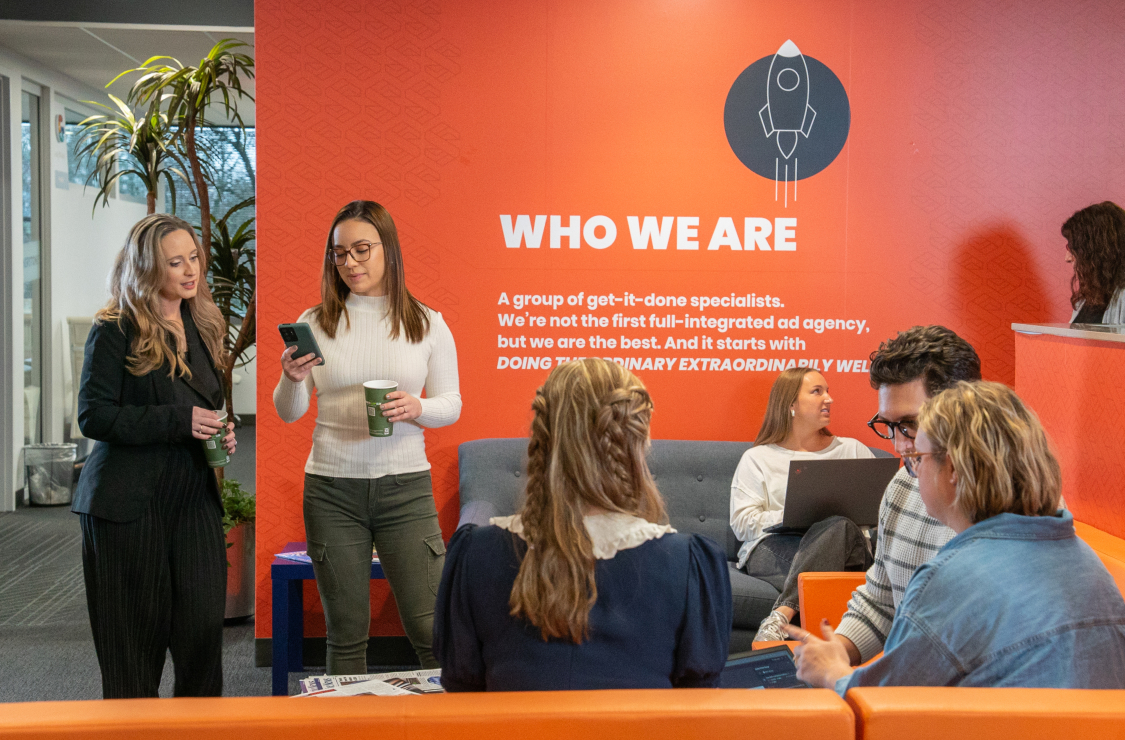 Stream employees gathered with laptops and phones in an orange-walled office
