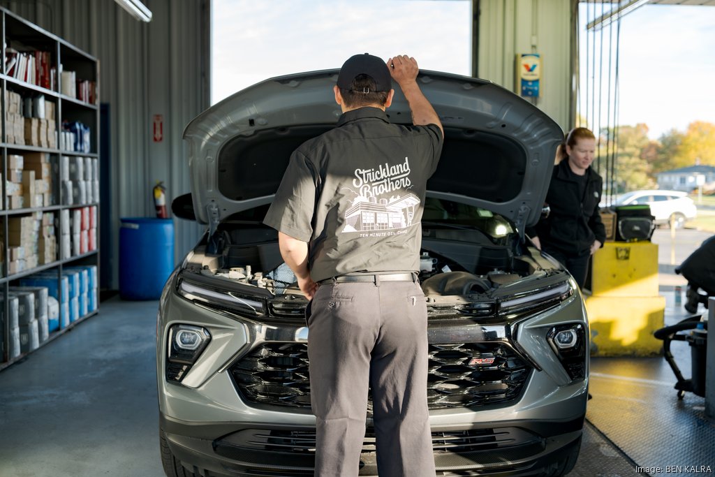 A Strickland Brothers technician working beneath the raised hood of a vehicle inside a service bay