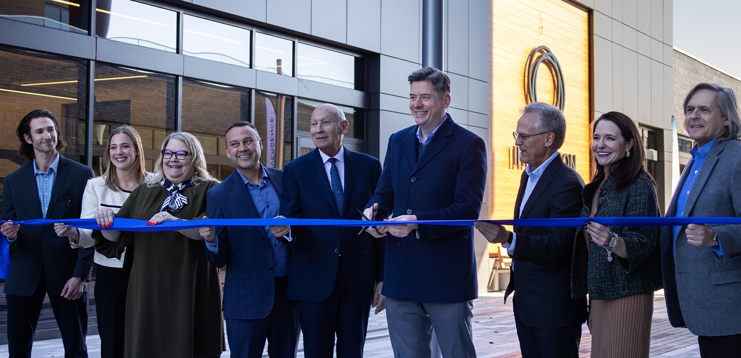 A group gathers outside a Stride Bank building to cut a blue ribbon.