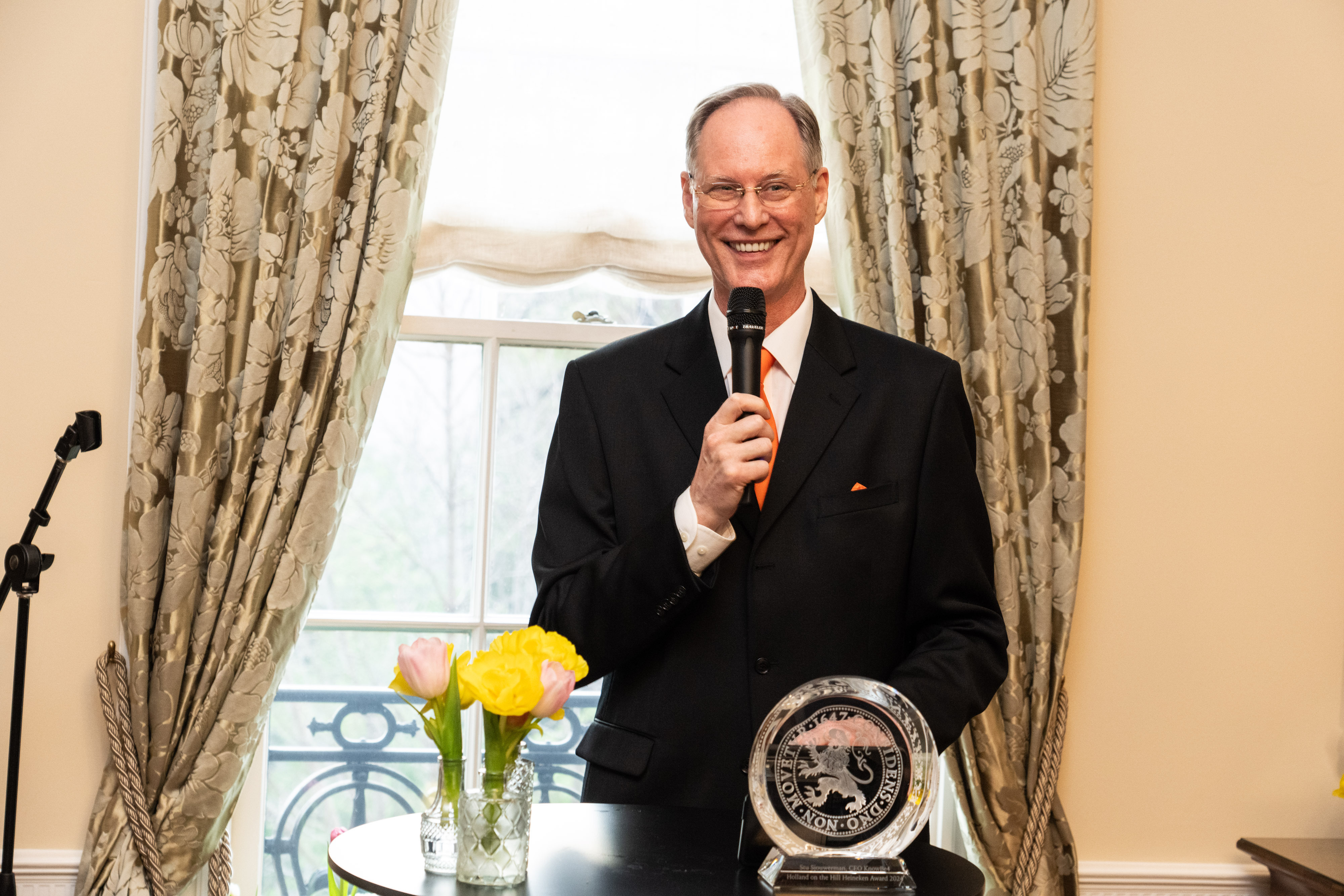 Stu Sjouwerman speaking beside his Freddy Heineken Award and a vase of tulips at the Dutch ambassador’s residence in April 2024.
