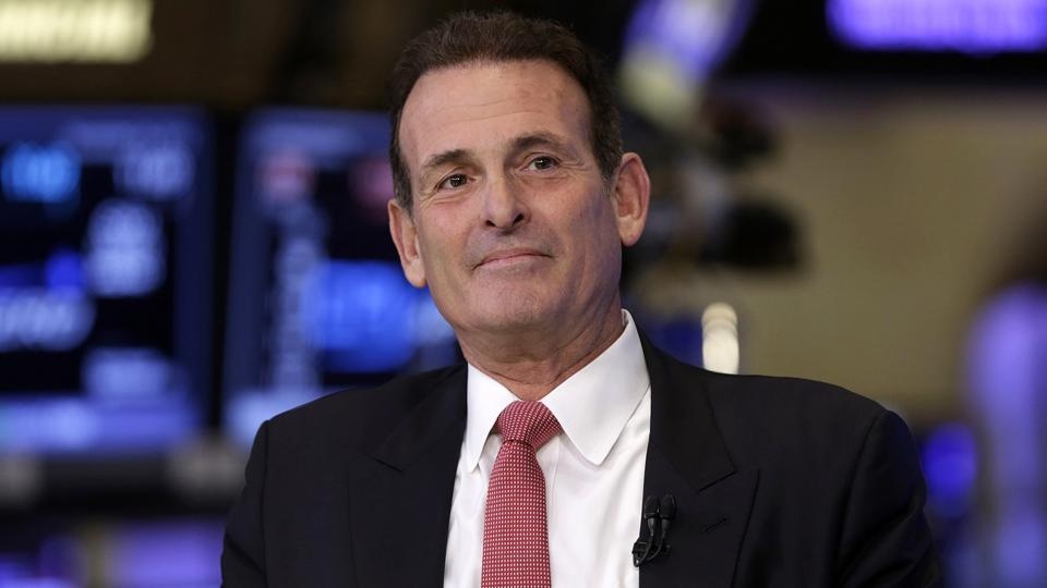 Stuart Miller in a suit and red tie, with financial-market screens behind him