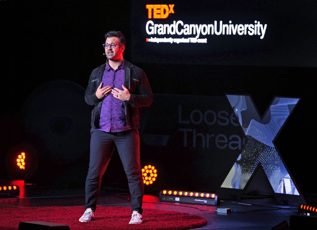 Michael Vilardo speaking on the red TEDxGCU stage in April 2025