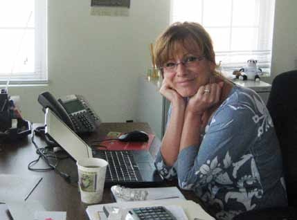 Archival photograph of Sue Welch seated at her desk beside a laptop and office telephone