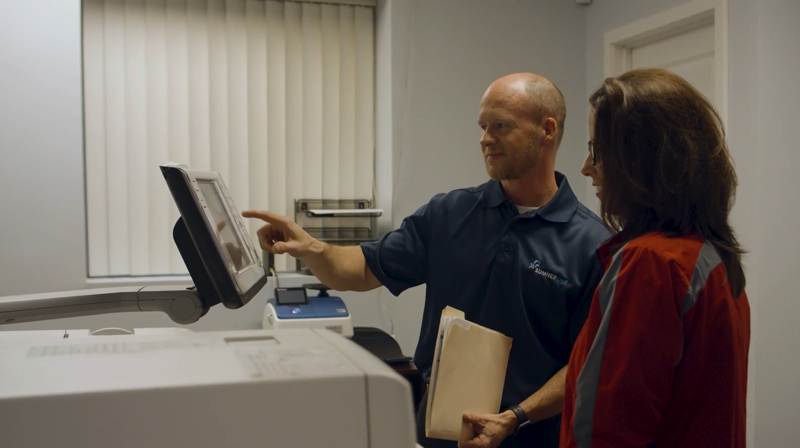 A SumnerOne staff member explaining a printing machine’s touchscreen to another person