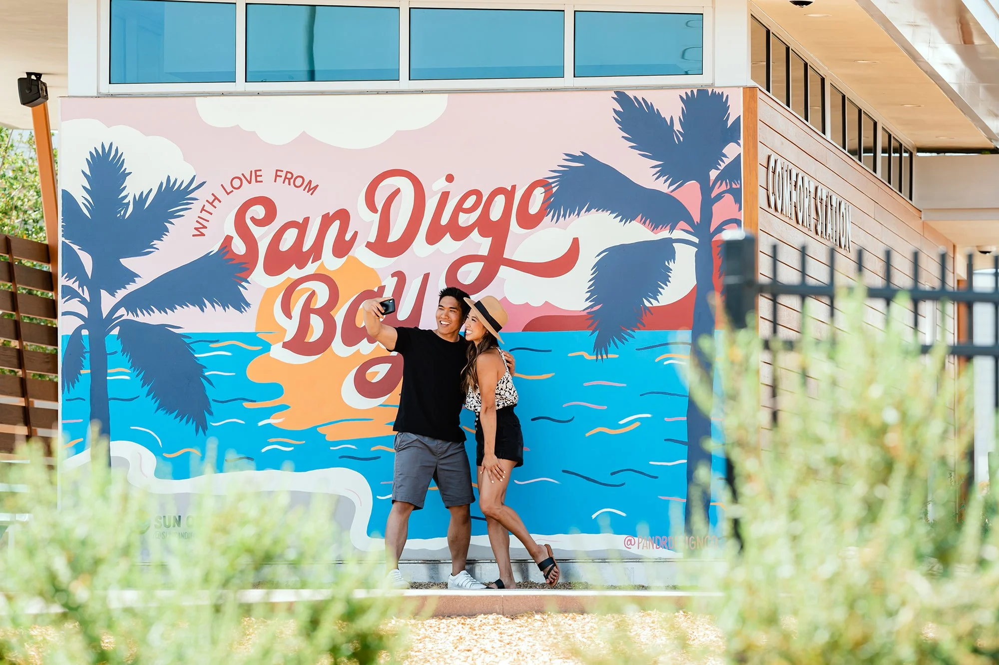 Two guests pose for a selfie at the colorful San Diego Bay mural at Sun Outdoors