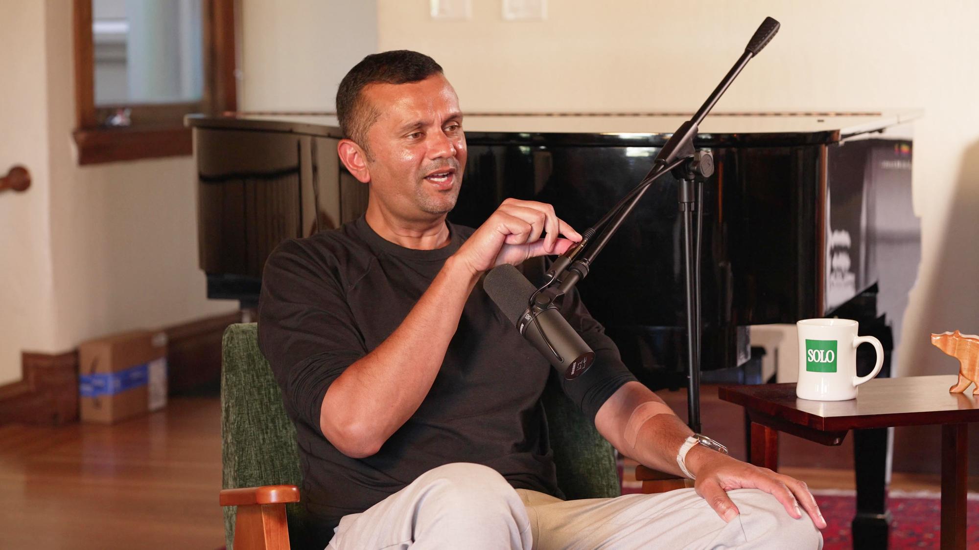 Sunil Rajaraman seated beside a piano, speaking into a microphone during the Solo Founders interview