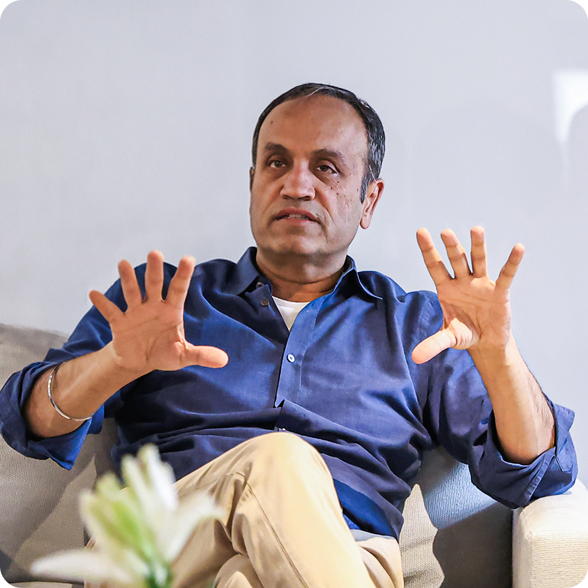 Sunny Singh seated in a blue shirt, speaking with both hands raised