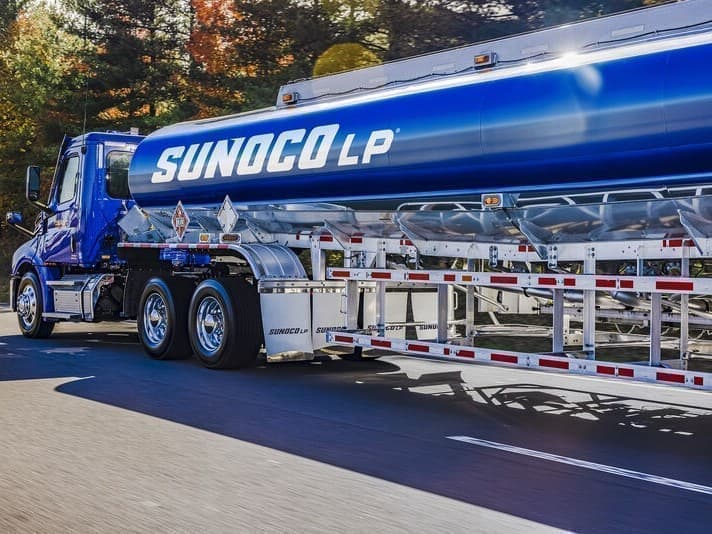 A blue Sunoco LP tanker truck travelling along a tree-lined road