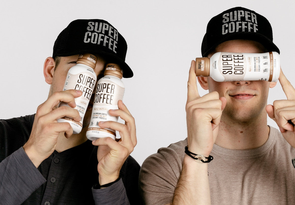 Two DeCicco brothers wearing Super Coffee caps and holding bottles in front of their faces