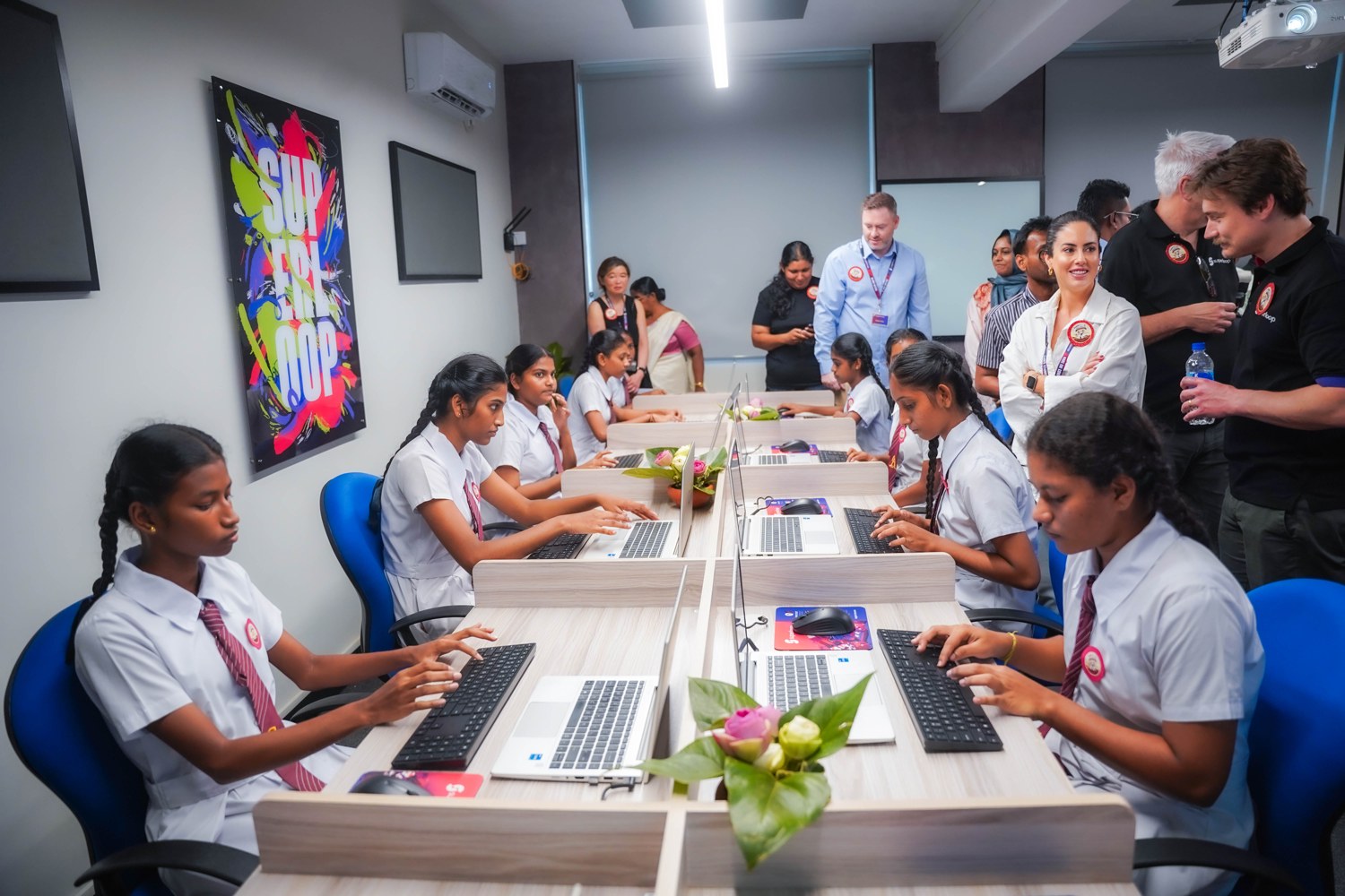 Students using laptops at the Superloop Future Minds Lab opening in Colombo, with staff and visitors standing behind them