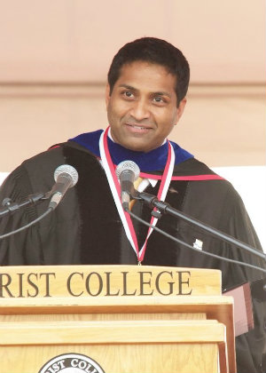 Suresh Kothapalli at the Marist commencement lectern, wearing academic regalia and the alumni medal