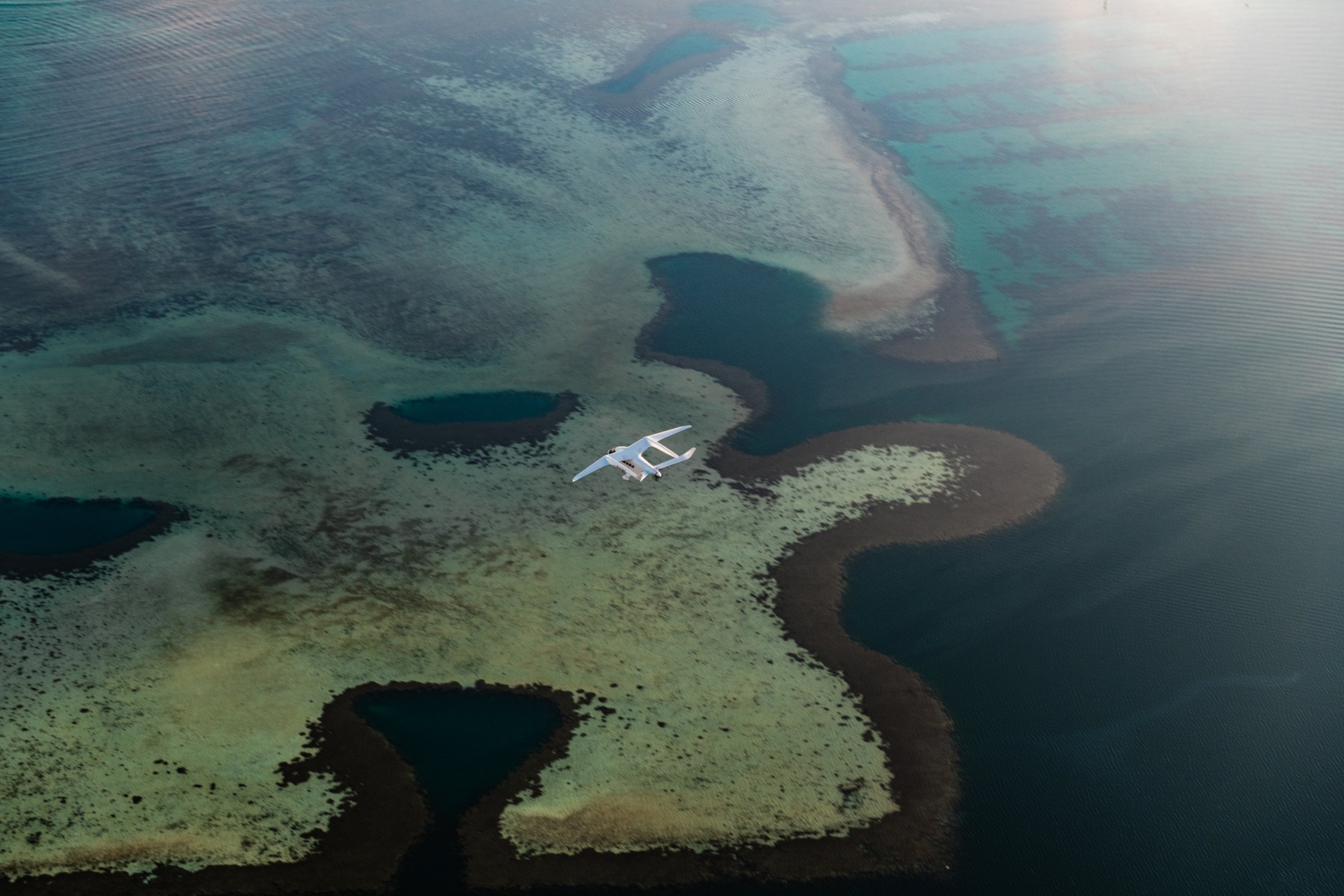 A BETA ALIA aircraft flies above patterned reef waters in Hawaii