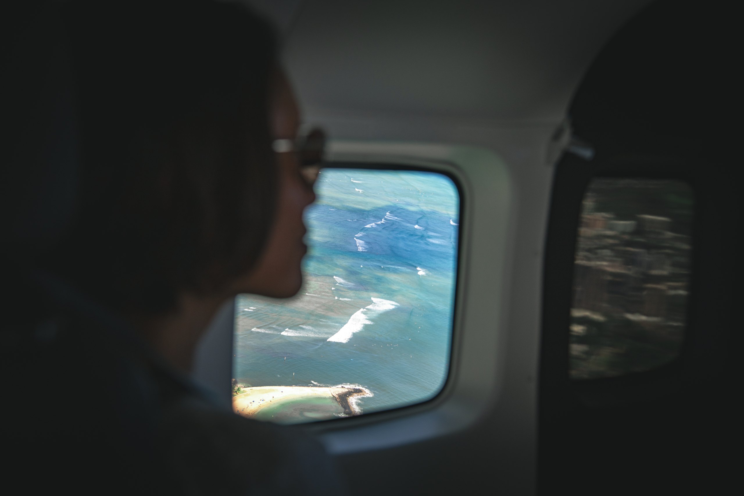 A passenger looks through a Mokulele aircraft window at the Hawaiian coast