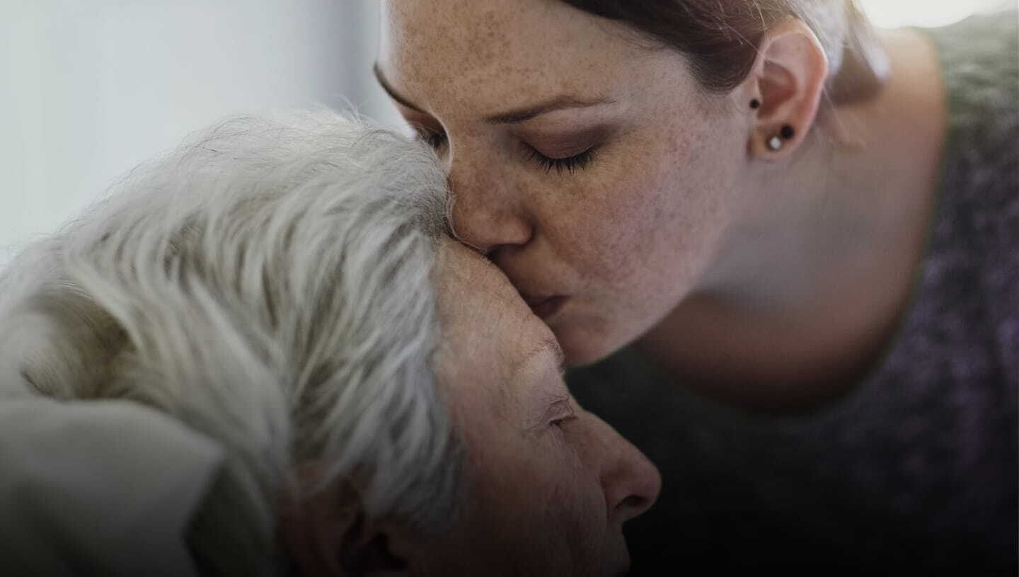 A woman gently kissing the forehead of an older patient