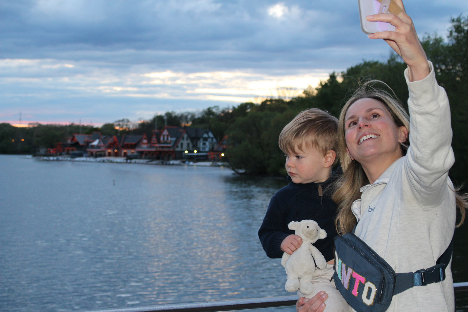 Suzie Devine holding a child beside the water while raising a phone for a photograph