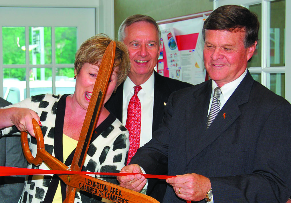 Montgomery, right, holding a red ribbon at a ribbon-cutting ceremony with Lexington Area Chamber of Commerce scissors