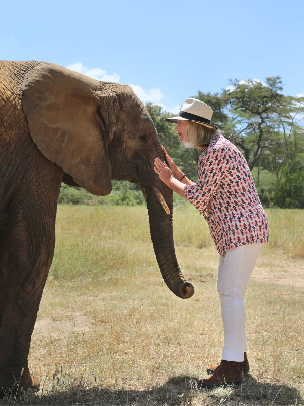 Sylvie Chantecaille wearing a hat and floral shirt, standing beside an elephant in Africa