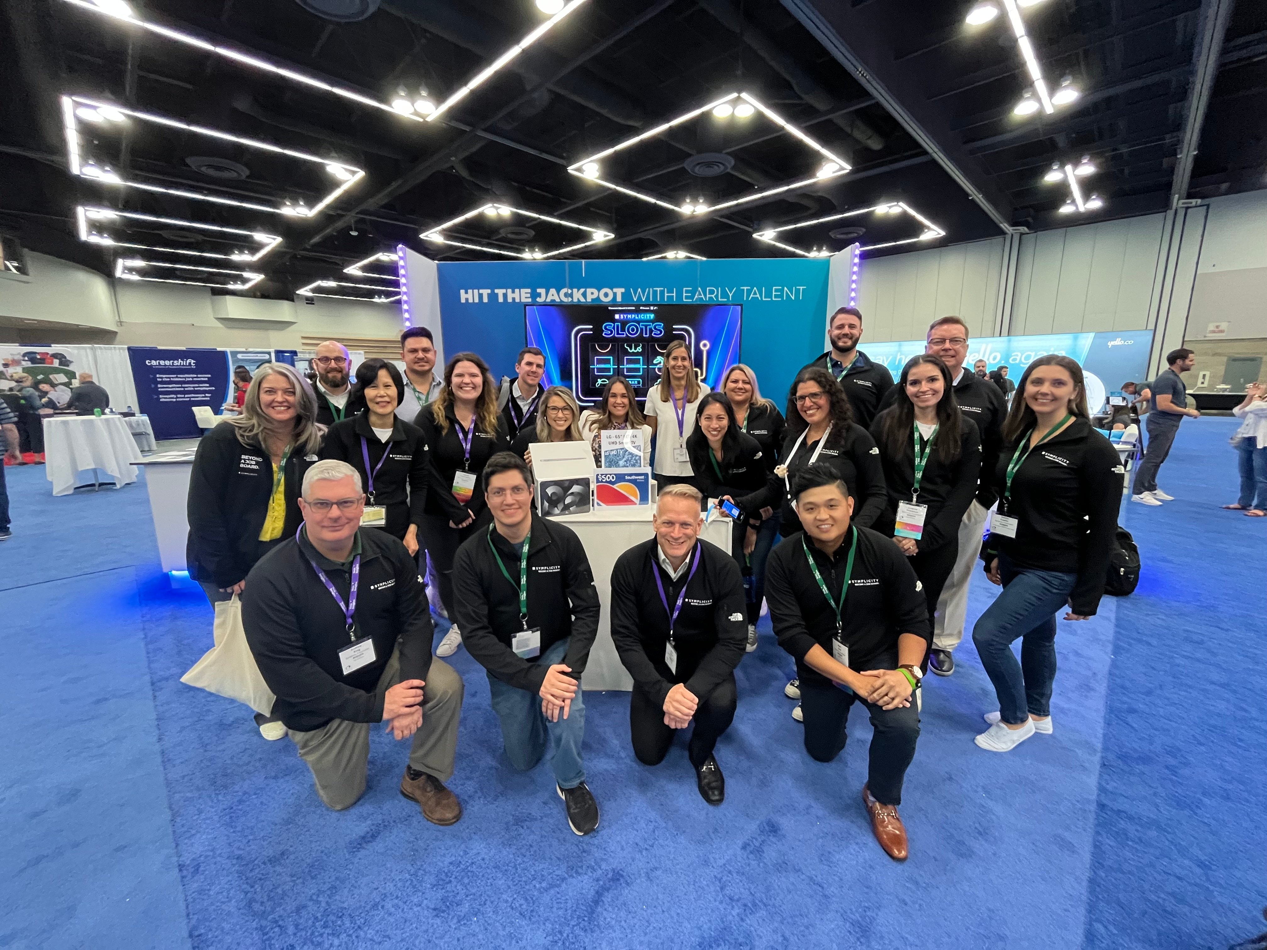 Symplicity team posing together at a trade-show booth themed around early talent recruiting