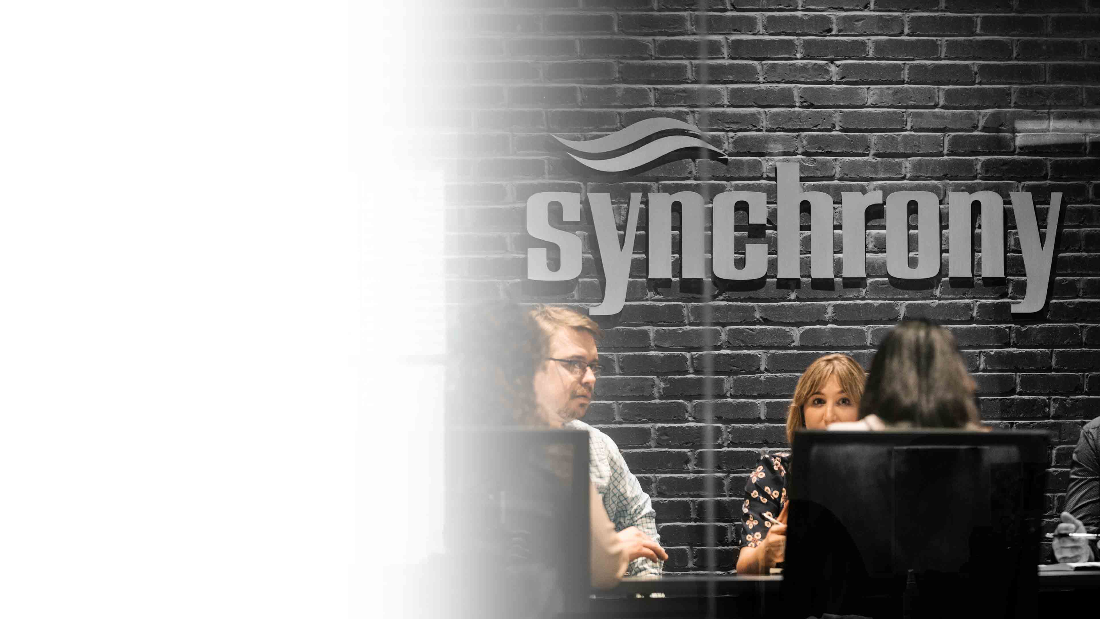 Synchrony colleagues meeting in front of the company wordmark in its West Chester office