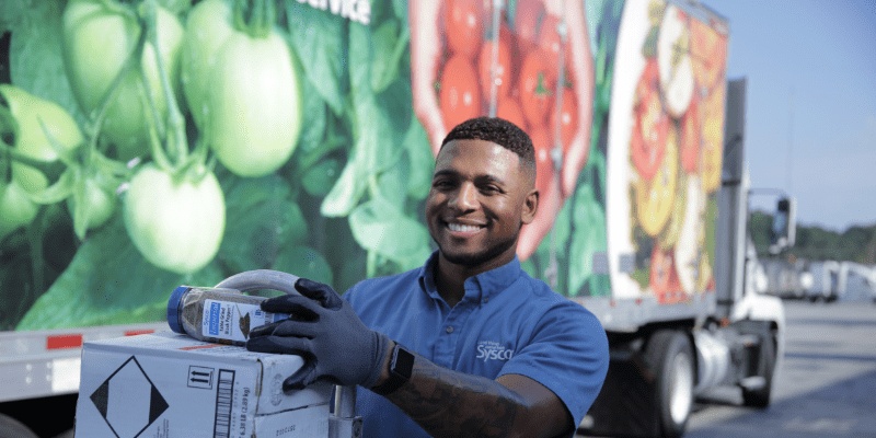 A Sysco delivery driver holding a box beside a refrigerated truck