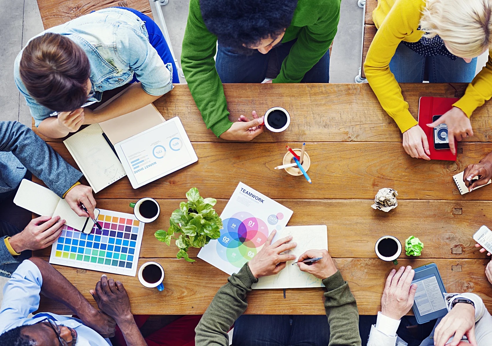 An overhead view of people working together around a wooden table