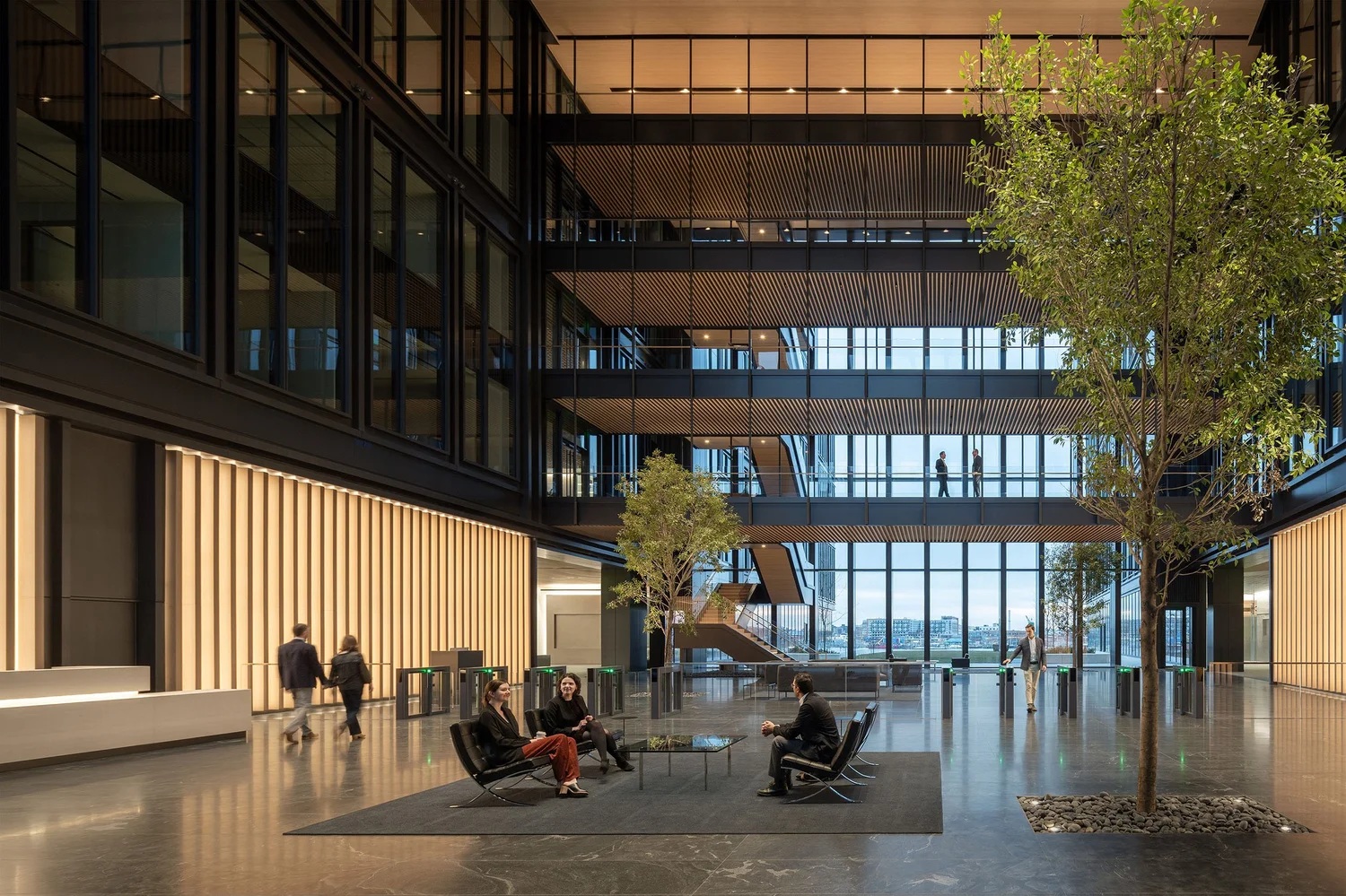 The atrium at T. Rowe Price’s headquarters, with seating, indoor trees and views toward the Baltimore waterfront