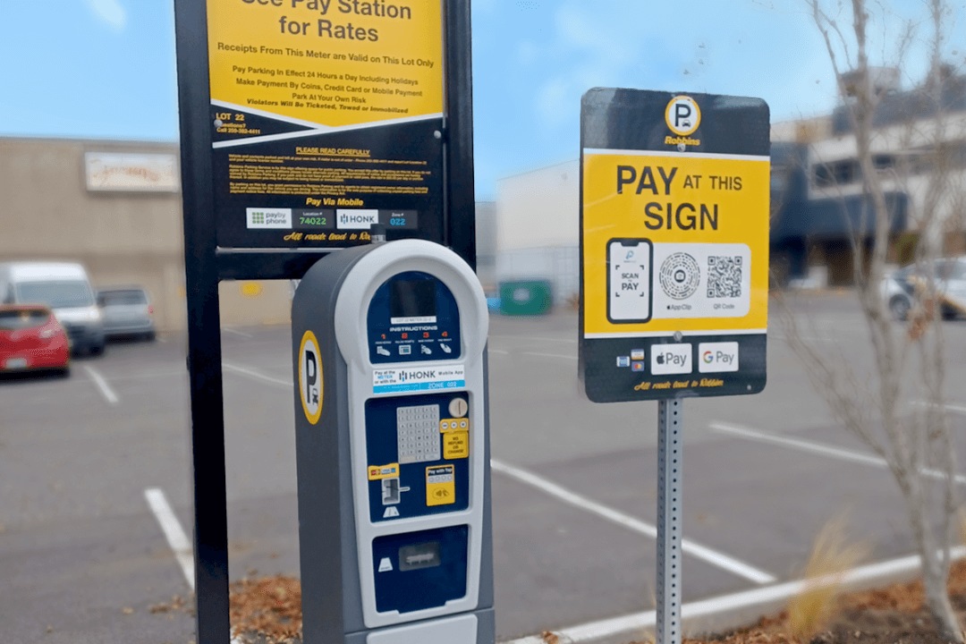 Robbins Parking pay station beside a yellow mobile-payment sign in a surface parking lot