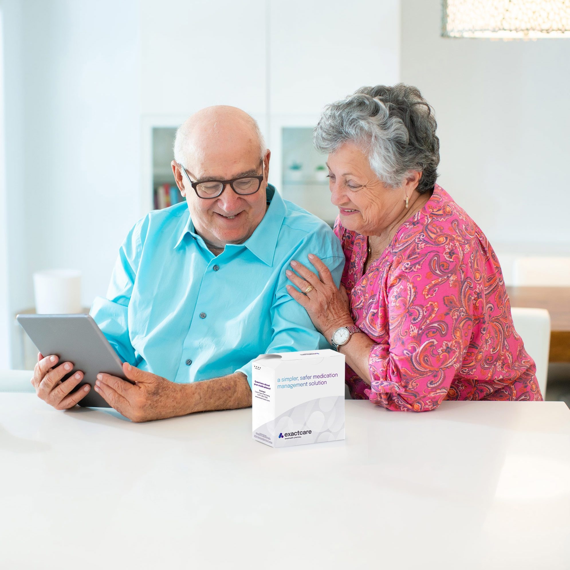 An illustrative older couple at a table with an ExactCare medication-packaging box