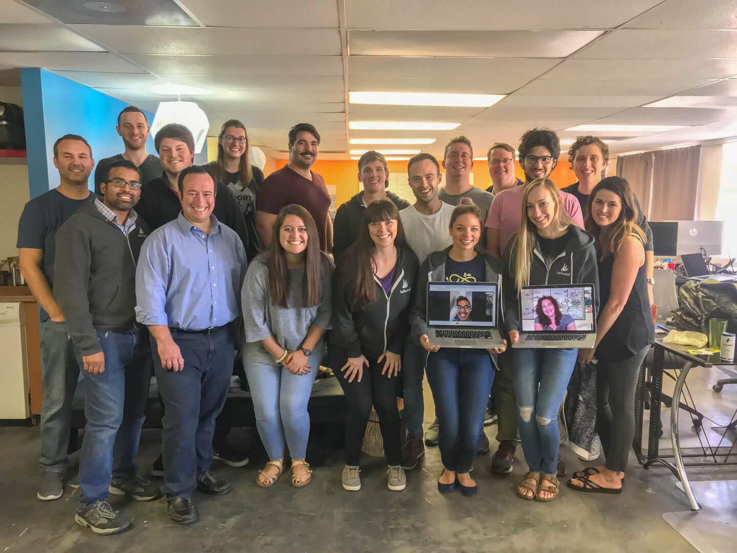 The Tailwind team gathered in their office, with two remote teammates joining on laptops held up in the front row.