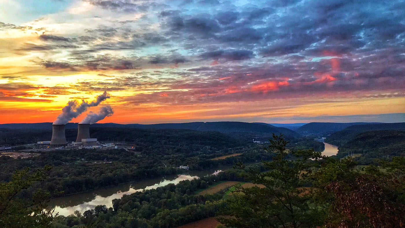 Susquehanna nuclear station and its two cooling towers beside a wooded river under a colorful evening sky
