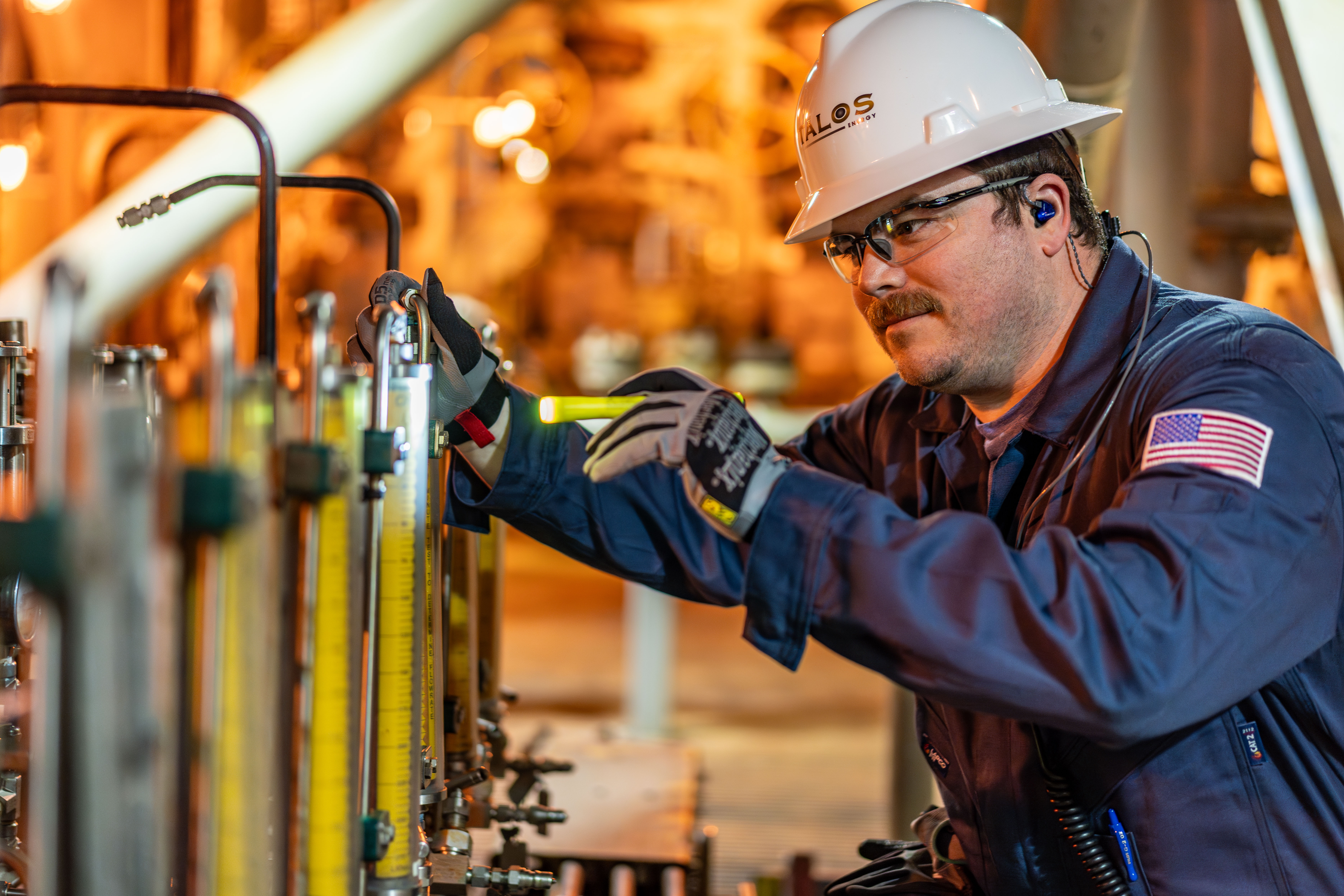 A Talos offshore worker wearing safety glasses, hearing protection and a hard hat while checking equipment