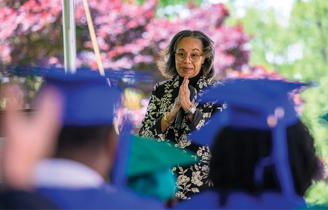 Tamla Olivier speaking to an audience with blue graduation caps in the foreground