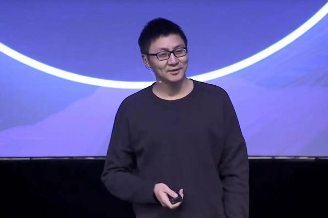 Tang Binsen speaking on stage in a black sweater and glasses